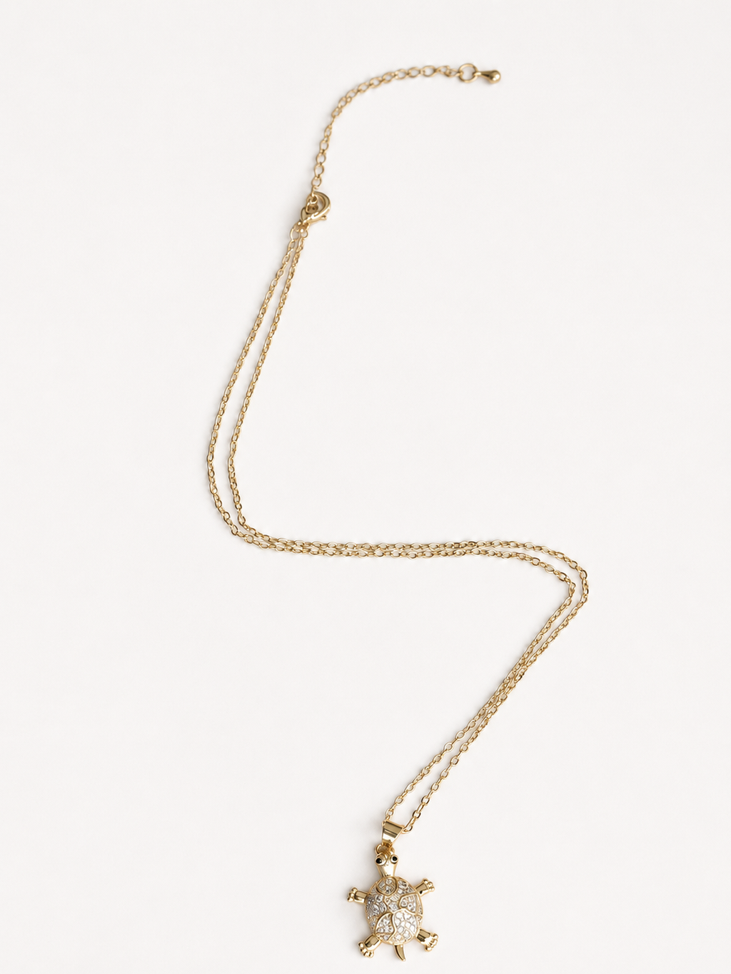 A gold chain necklace featuring a small turtle pendant adorned with clear rhinestones, displayed on a clean white background.