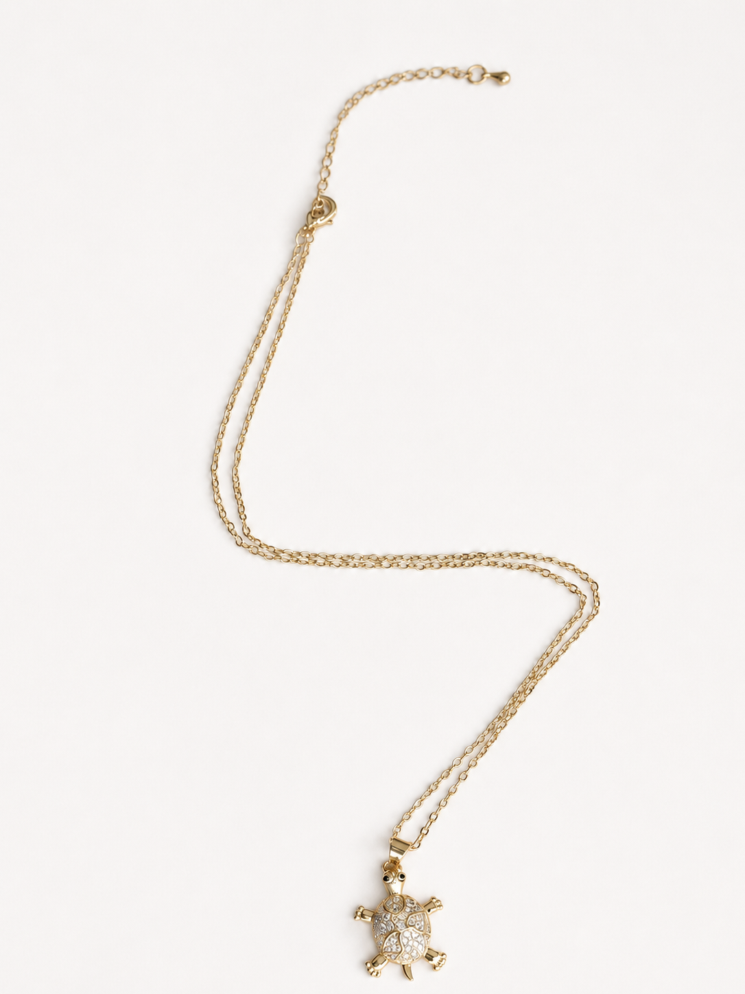 A gold chain necklace featuring a small turtle pendant adorned with clear rhinestones, displayed on a clean white background.